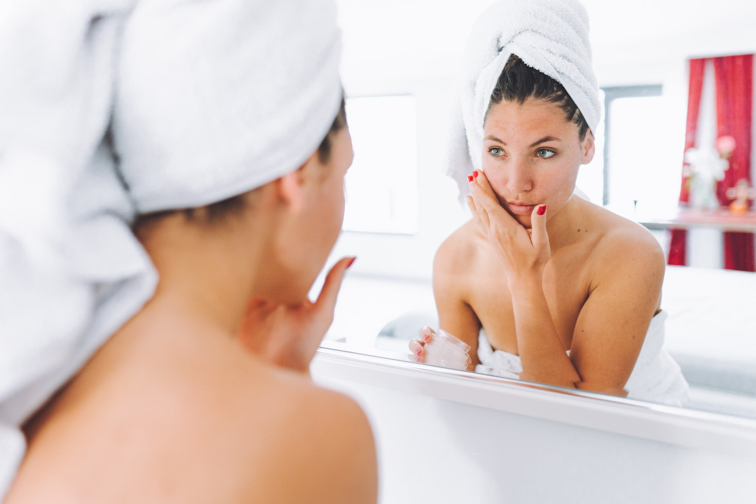 Face care routine, applying nourishing lotion and cream, female in towel taking time to admire face skin pampering in the mirror. Waist up